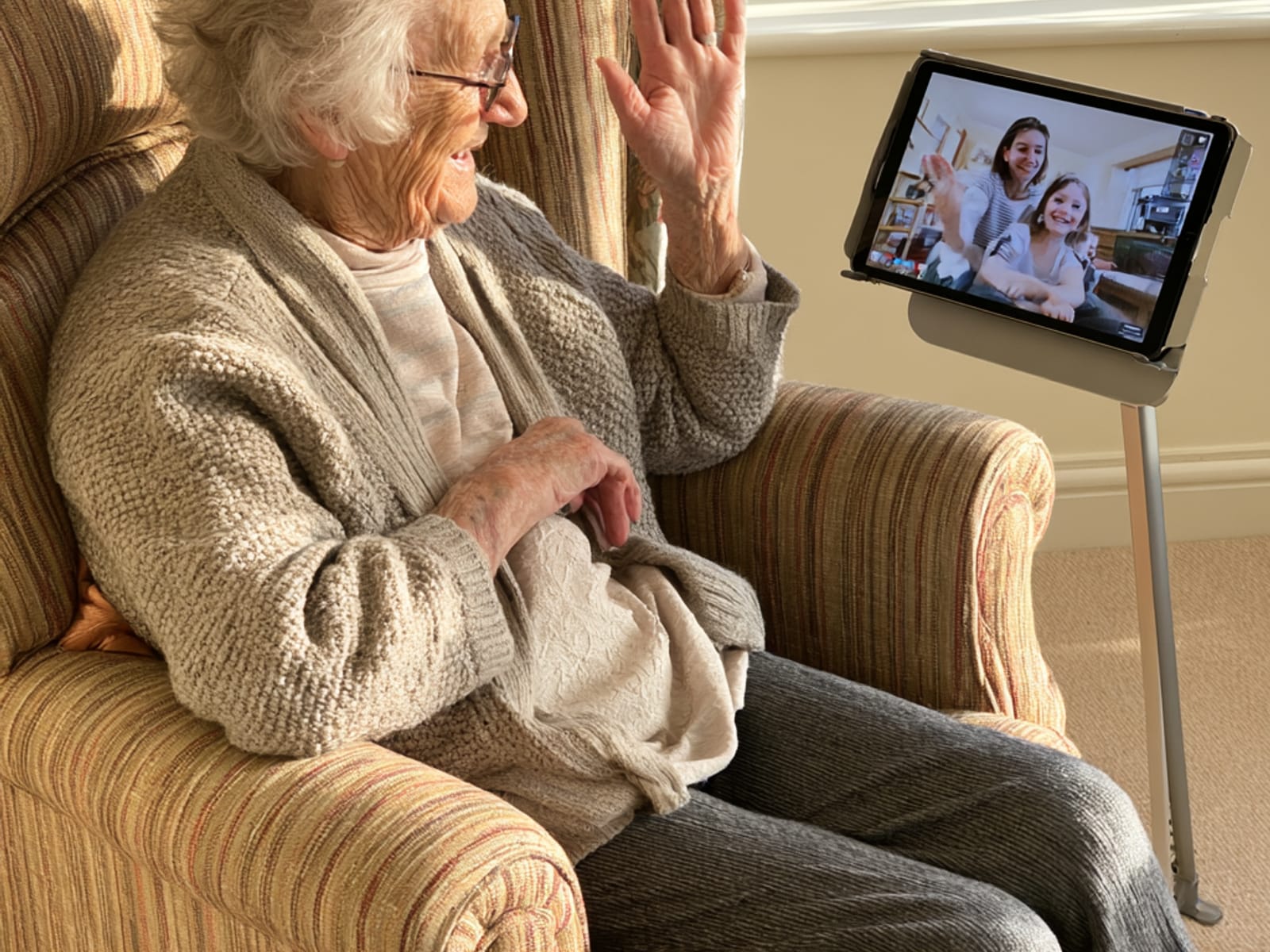 Eine ältere Frau winkt ihren Enkeln in einem Videoanruf auf dem Tablet zu.